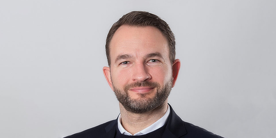 Porträt des OEV-Mitarbeiters Daniel Spiecker im Anzug, der freundlich in die Kamera blickt